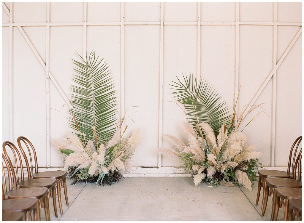 White barn wedding ceremony with palms and pampas grass
