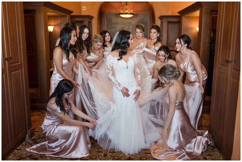 bridesmaids in blush satin gowns helping bride into dress at Bella Collina