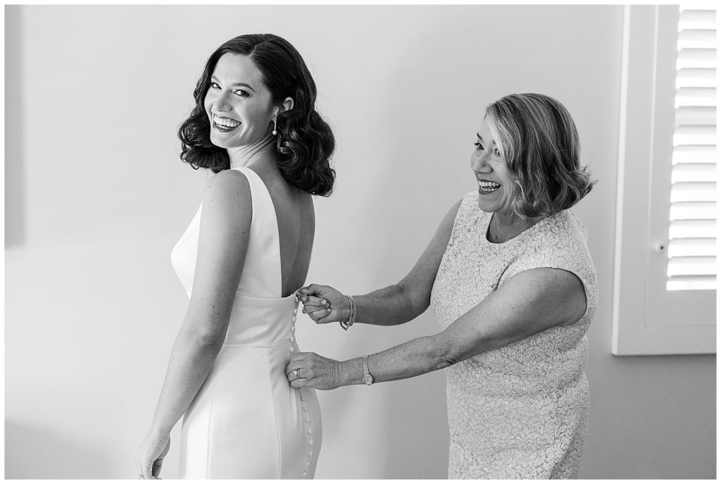 bride putting on wedding dress with help of her mom